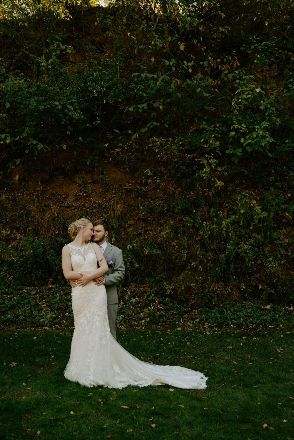 Romantic outdoor wedding portrait against lush green foliage backdrop.