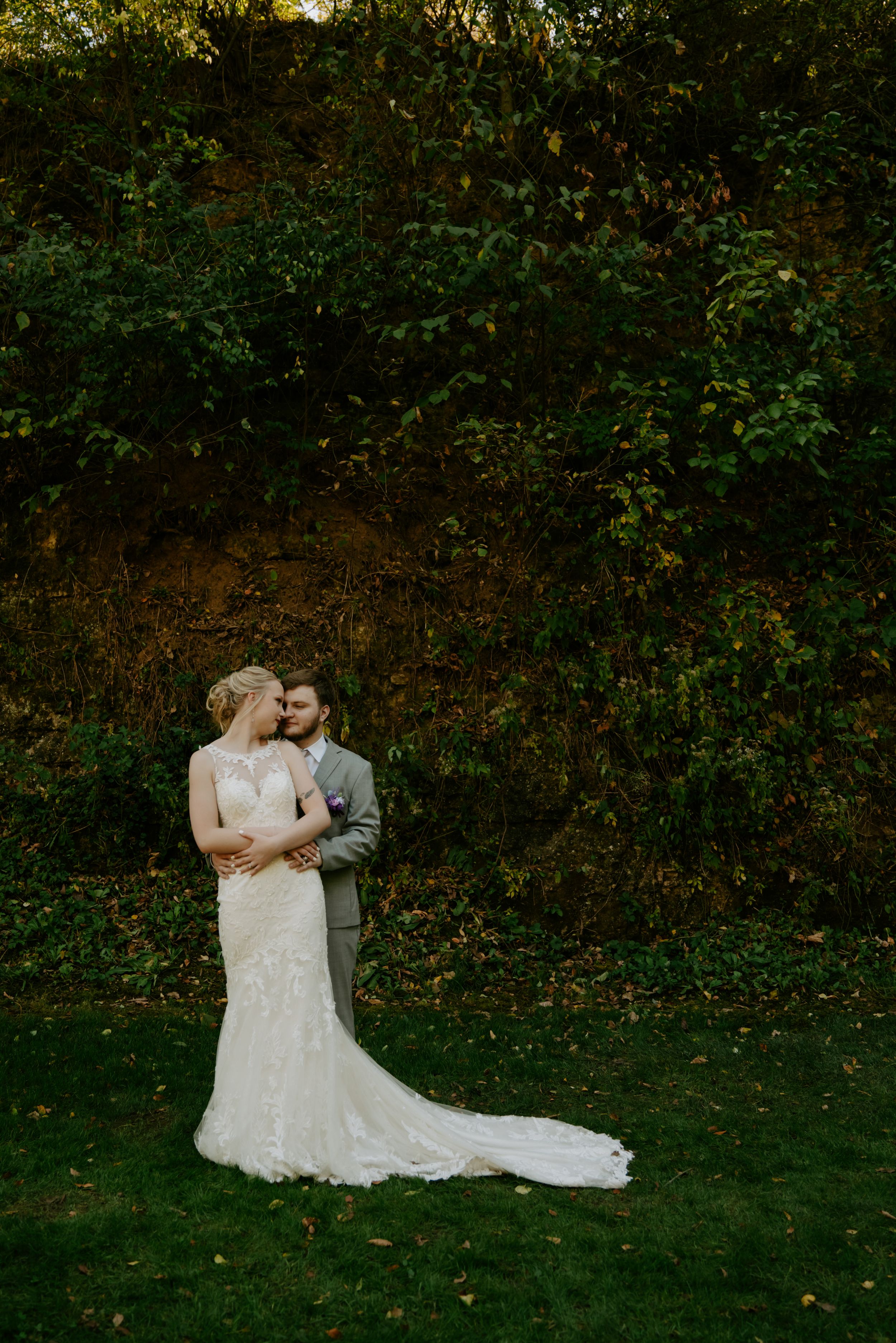Romantic outdoor wedding portrait against lush green foliage backdrop.