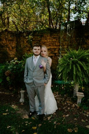 A romantic wedding photoshoot in front of a rustic brick wall with lush greenery and ferns.