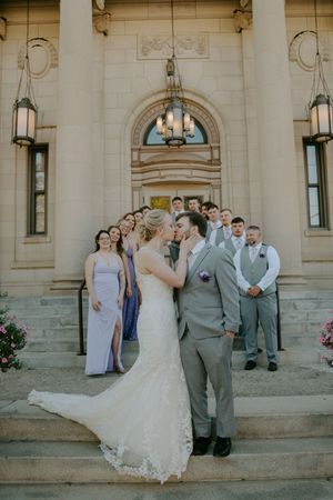 Wedding party poses on grand stone steps of a classical building with columns and archways.