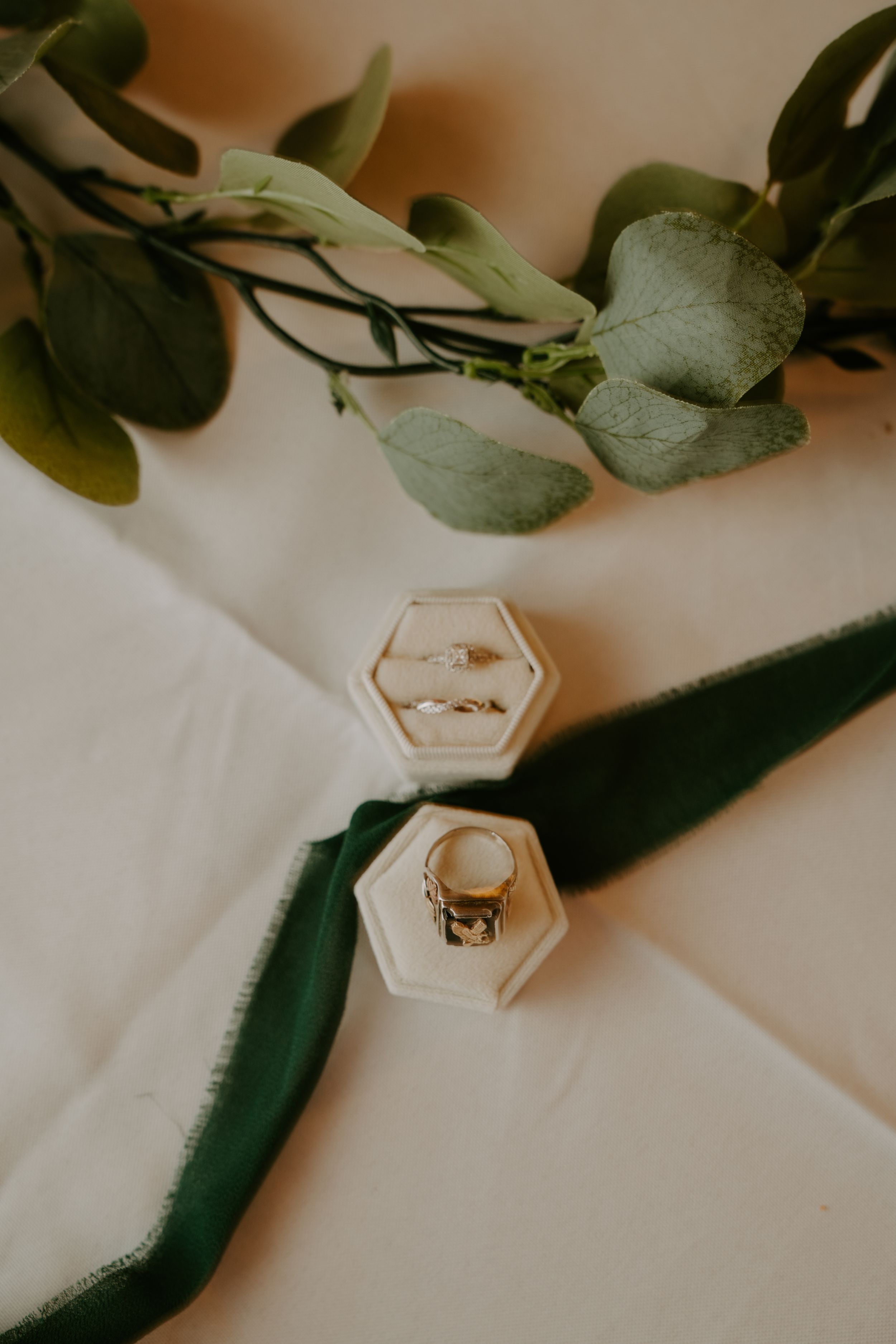 Wedding rings displayed in hexagonal box with eucalyptus leaves and white fabric styling.
