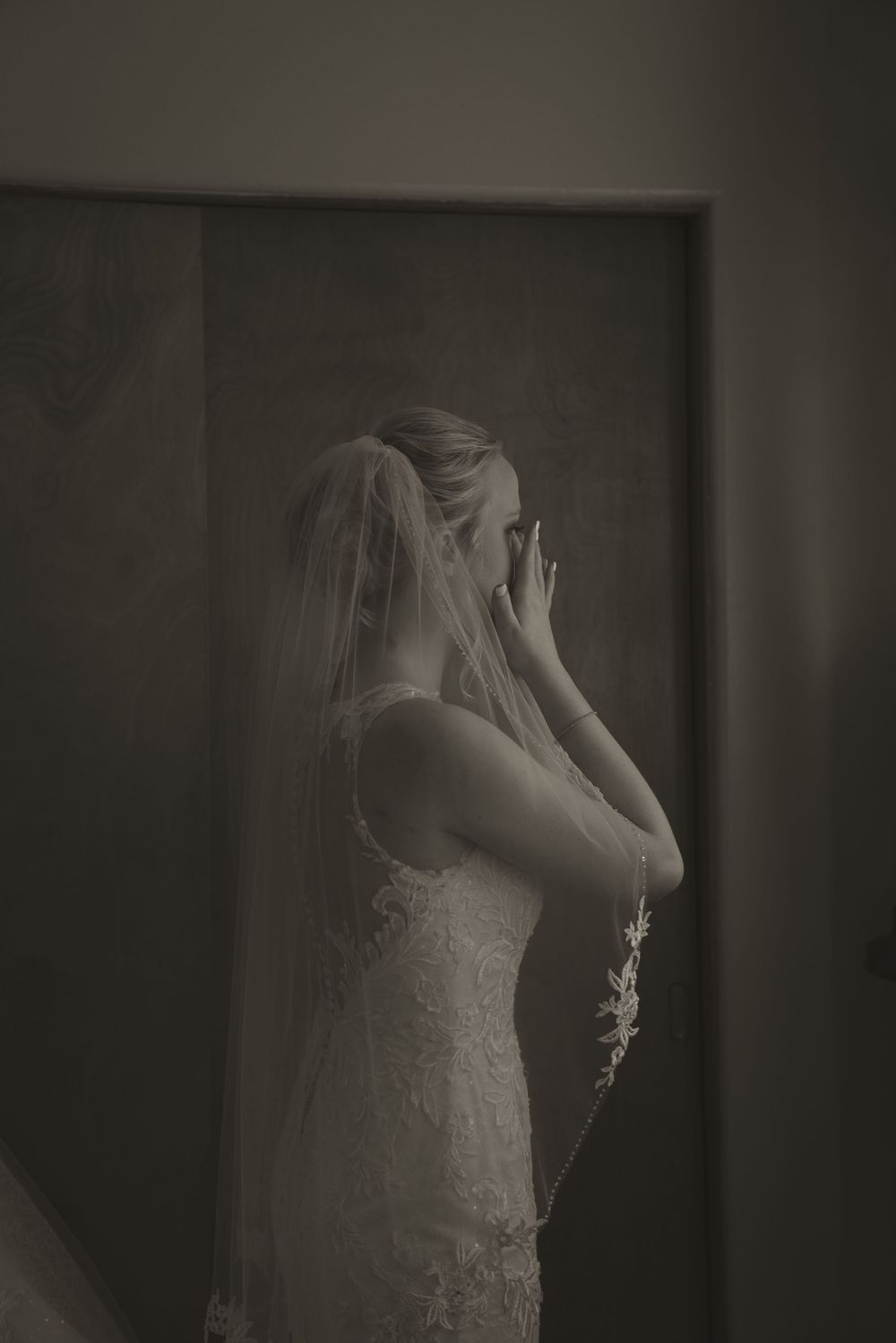 Moody black and white photo of bride adjusting veil before ceremony.