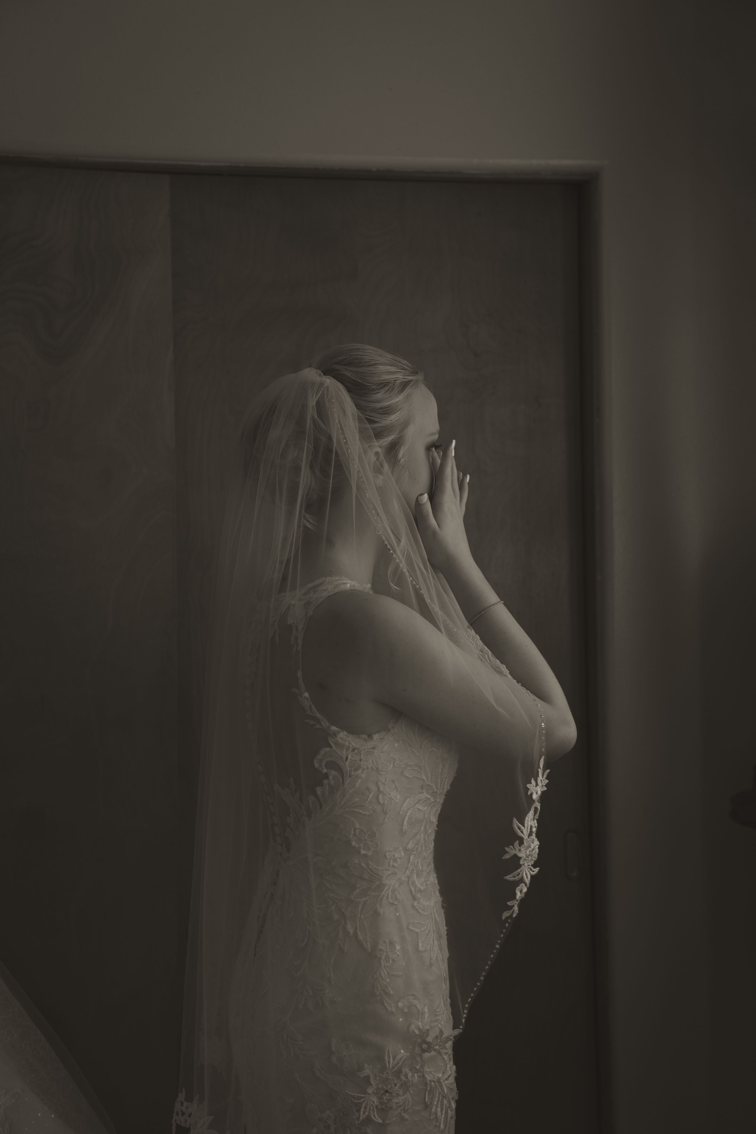 Moody black and white photo of bride adjusting veil before ceremony.