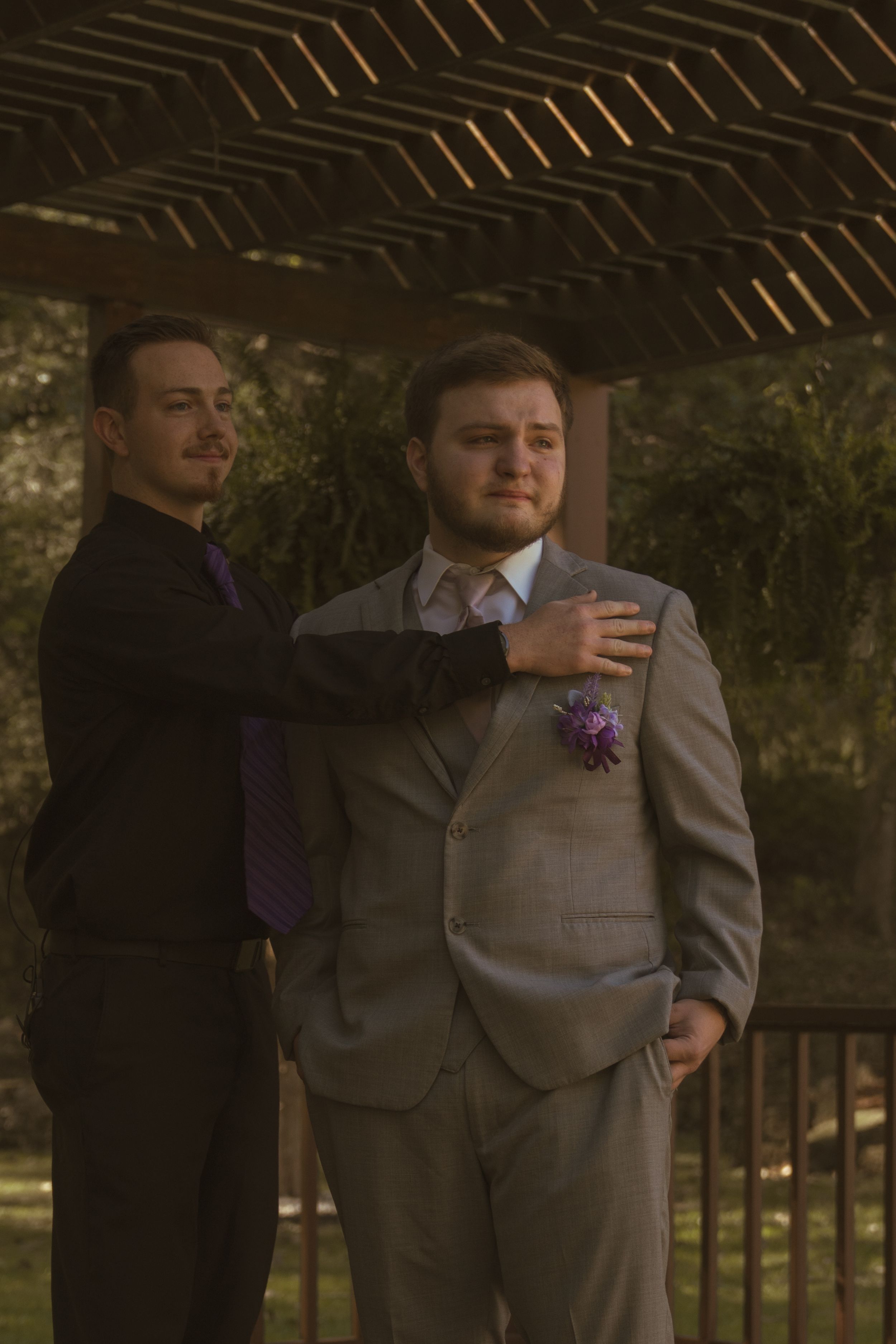 Wedding party members in gray suits helping with final adjustments outdoors.