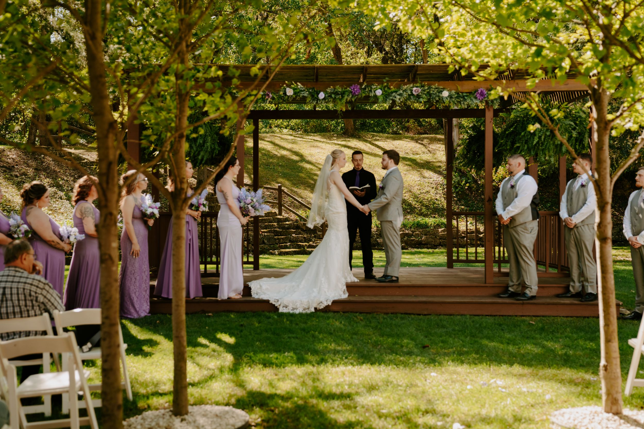 Panoramic view of outdoor wedding ceremony under tree-lined pathway.