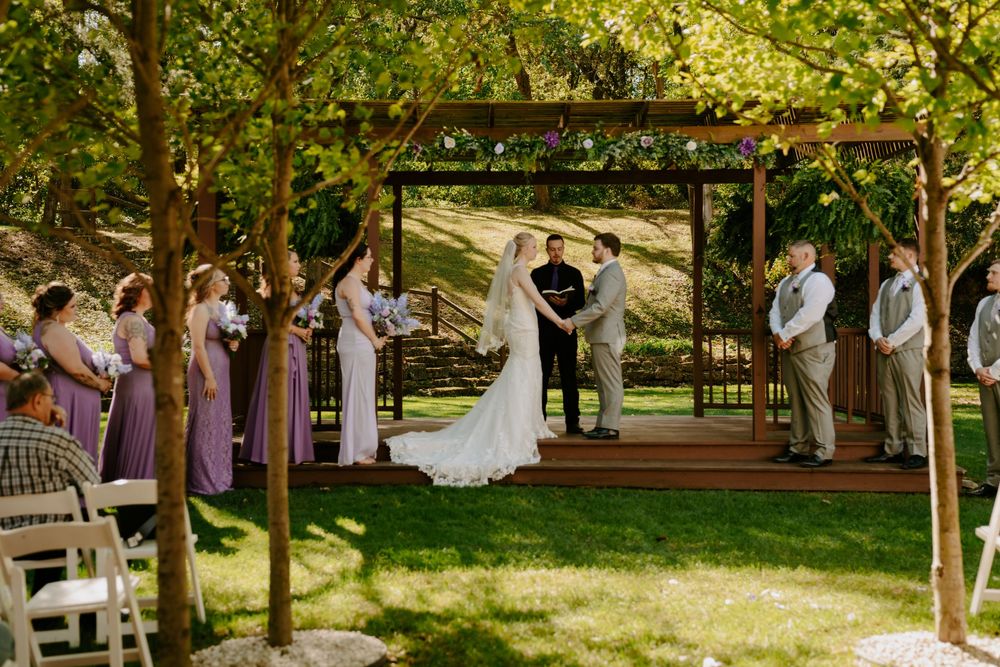 Panoramic view of outdoor wedding ceremony under tree-lined pathway.
