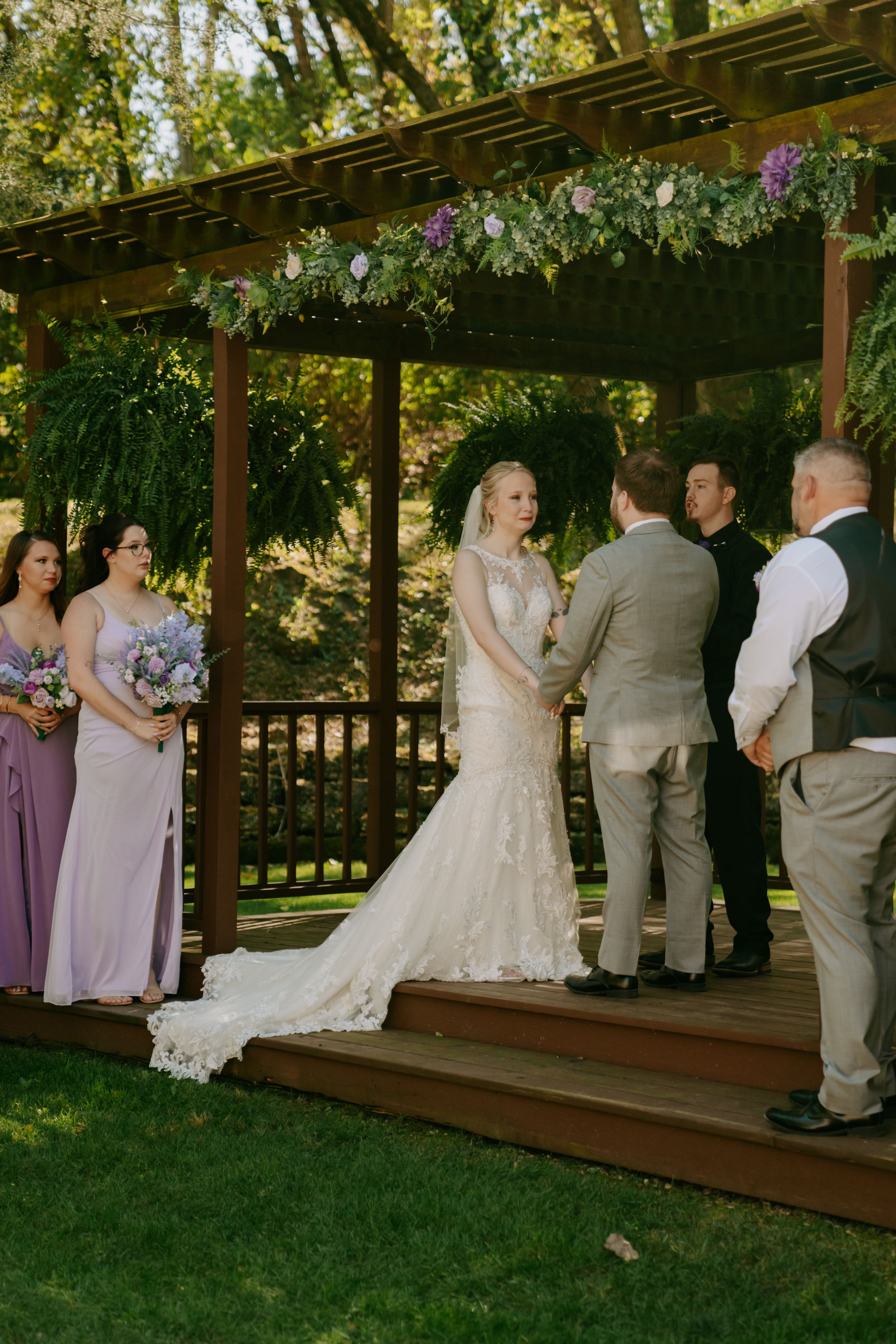 Wedding party lined up under wooden pergola decorated with flowers.