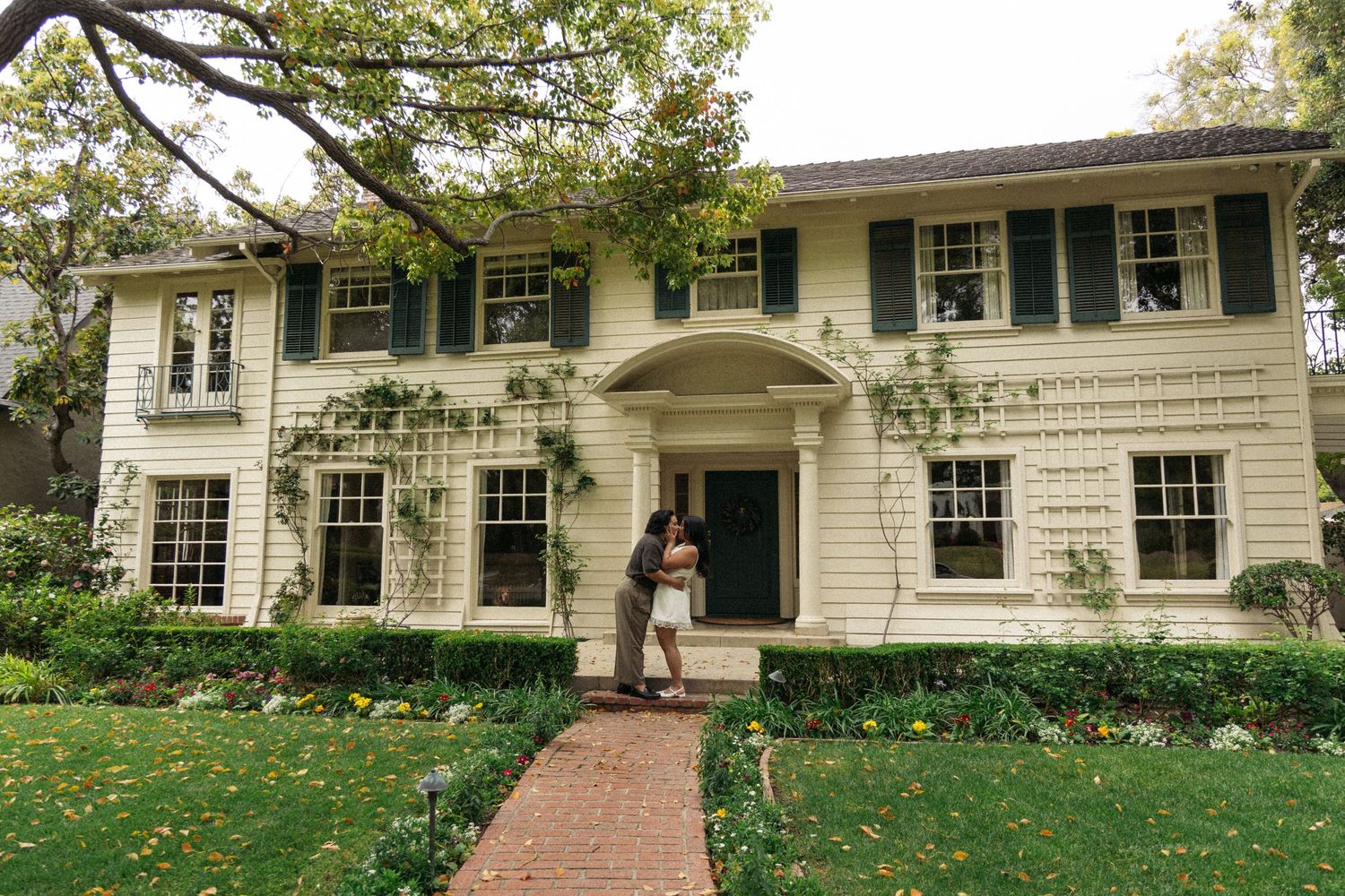 Classic white colonial house with green shutters and manicured landscaping on a fall day.