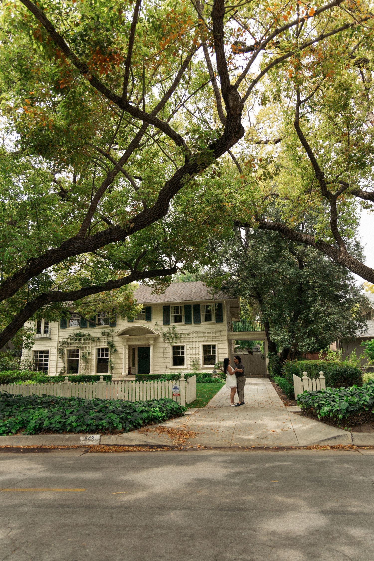 Exterior view of a charming colonial-style house with white siding and green trees in the landscaping.