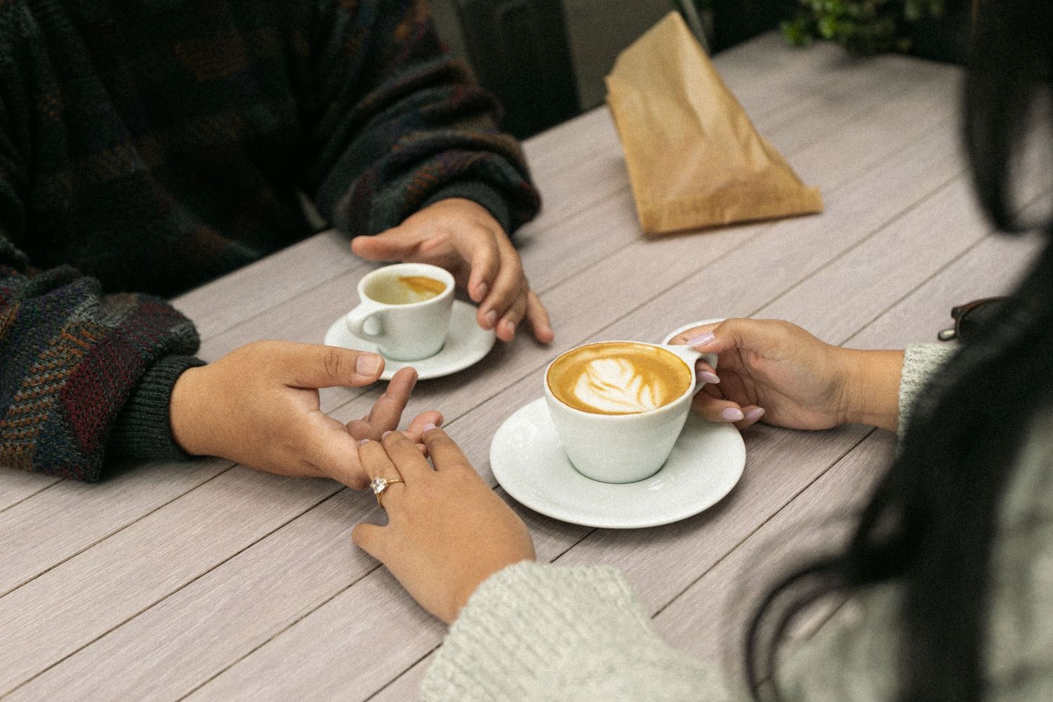 Two people enjoying coffee with latte art at an outdoor wooden table on a cozy afternoon.