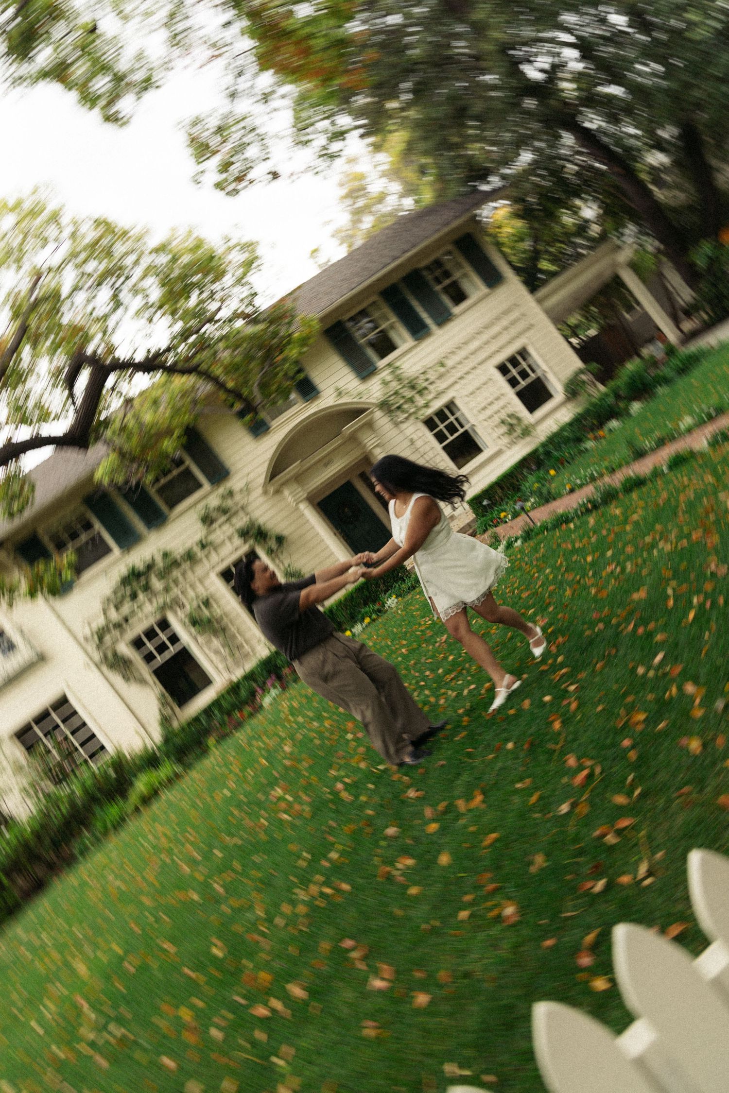 White colonial house with a sprawling green lawn scattered with orange autumn leaves.