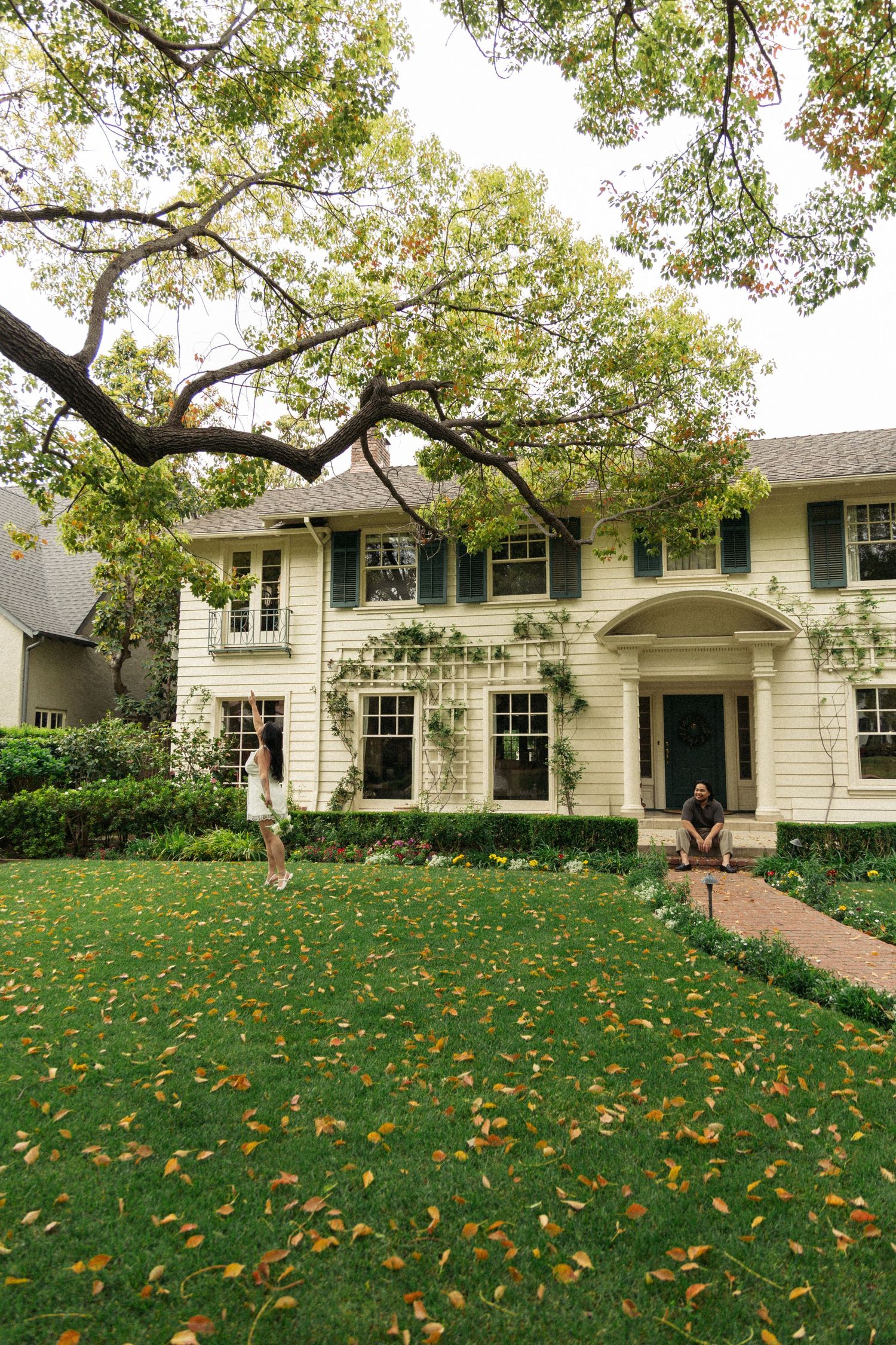 Elegant white colonial mansion with manicured lawn and fall leaves scattered across the ground.