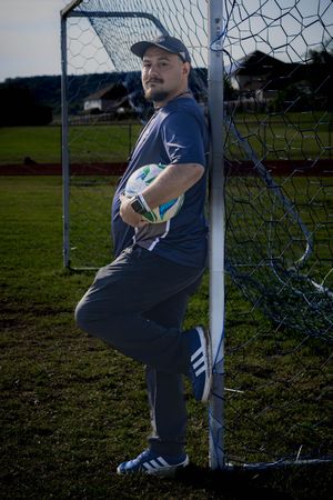 Soccer goalkeeper in navy attire leans against goal post during field practice session.