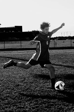 Black and white action shot of a soccer player mid-kick preparing to strike the ball on a grass field.