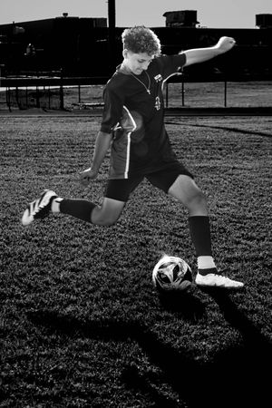Soccer player takes aim at a soccer ball during a dramatic black and white practice shot on a grass field.