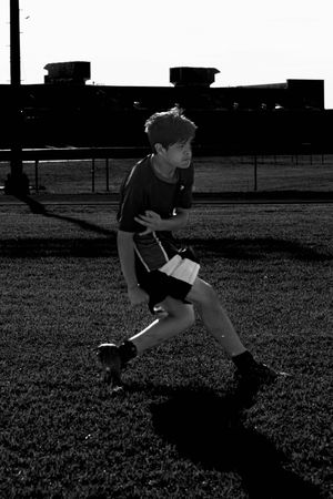 A soccer player practices footwork drills on a grass field in dramatic black and white contrast.