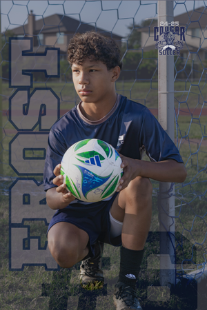 Young soccer player in navy uniform kneels by goal post holding blue and green soccer ball during practice session.