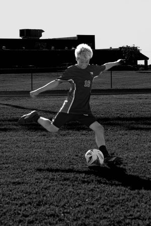 A soccer player dribbles a ball on a grassy field in black and white photography.