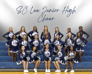 Cheerleaders in navy blue and white uniforms pose together on bleachers in a school gymnasium.