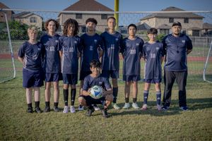 Youth soccer team in navy blue uniforms poses together on grass field in front of goal net during practice.