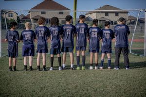 Soccer team players standing in a line on grass field wearing matching navy blue jerseys with numbers shown on their backs.