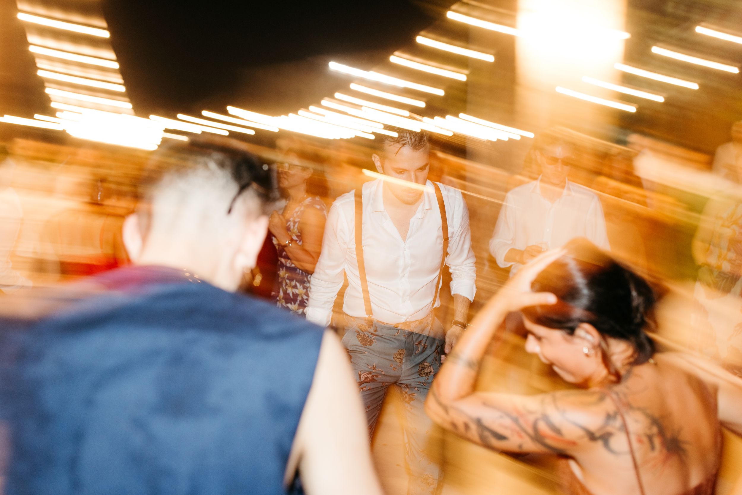 Blurred motion photo of people dancing at a dimly lit party with golden lighting creating a dynamic atmosphere.