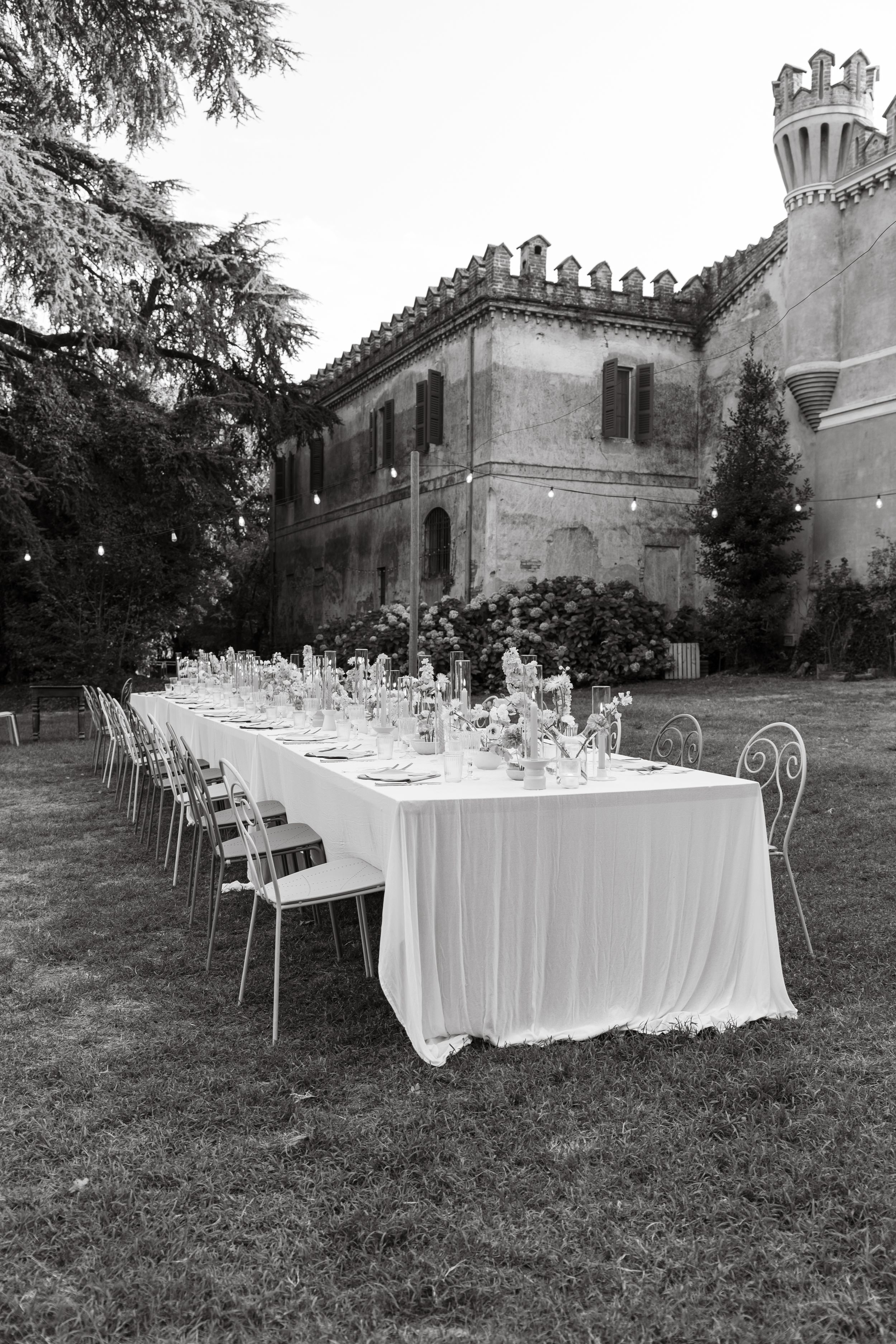 Long dining table with white tablecloth and elegant place settings set up outdoors at a castle venue for an elegant event.