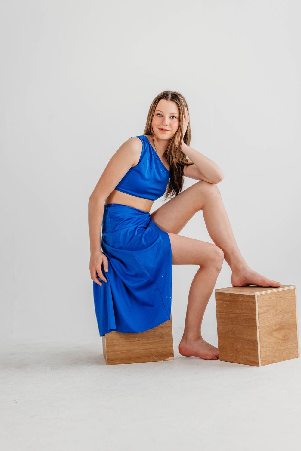 Model in royal blue two-piece outfit posing on wooden blocks against white backdrop for fashion photography.