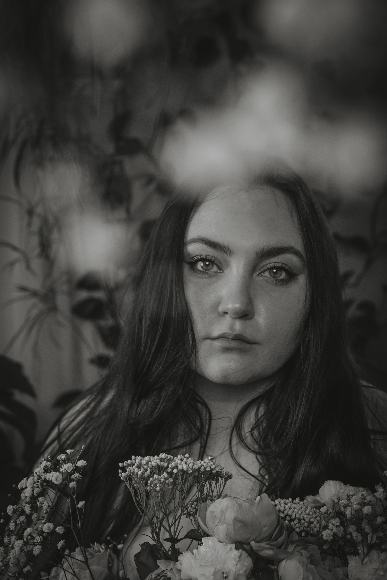 A black and white portrait series of a person surrounded by delicate white flowers and foliage in a dreamy setting.