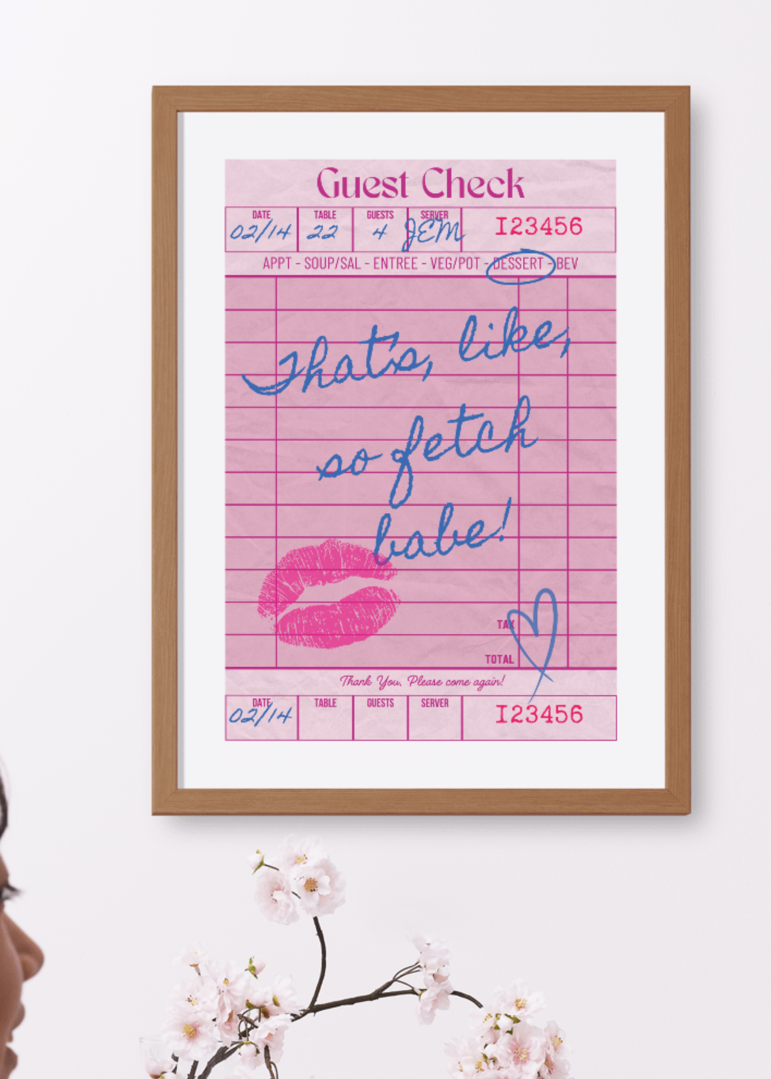 Framed pink guest check with handwritten text 'thats like so fetch babe' and a lipstick kiss mark in a wooden frame.