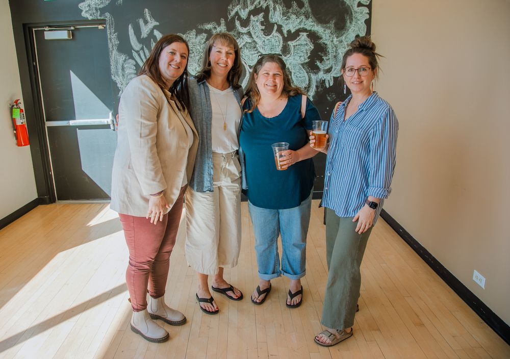 Four staff members stand together in a brightly lit hallway with hardwood flooring and gray walls.