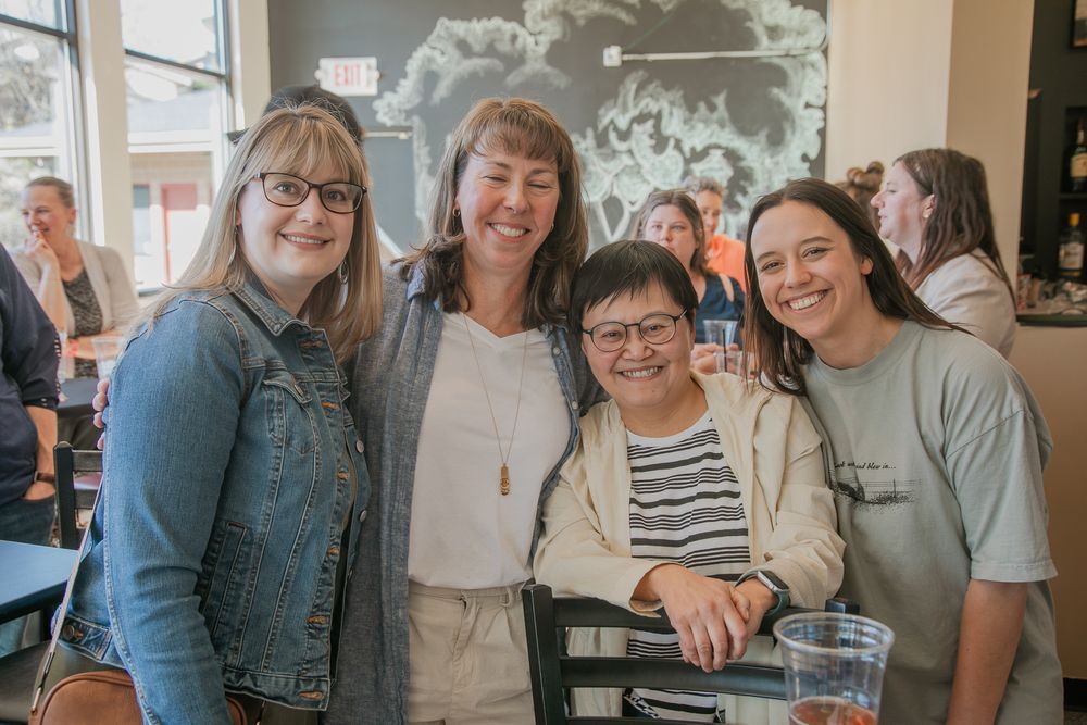 Four people gather together smiling at a casual dining venue with drinks and a relaxed atmosphere.