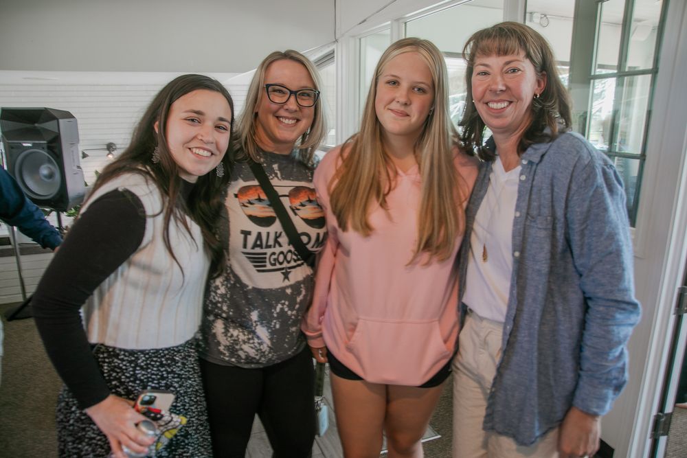 A group of friends posing together indoors wearing casual outfits including a pink sweatshirt and denim jacket.