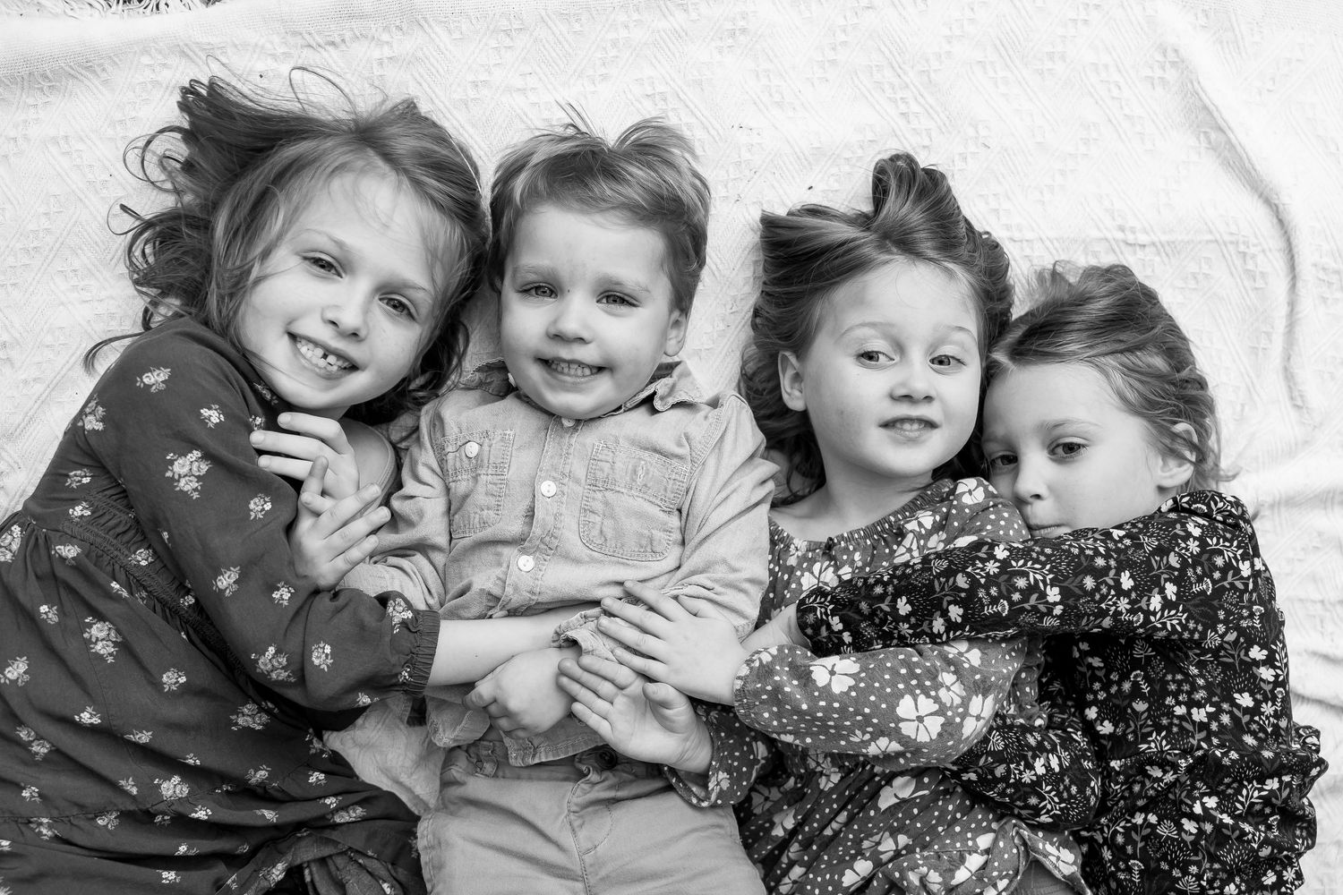 Four energetic children lying down together in winter clothing, captured in a black and white photograph.