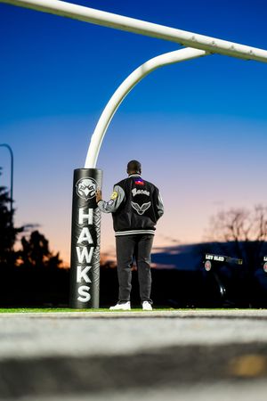 Silhouette of person standing next to an Nelson Hawks sign post against a blue and orange sunset sky.