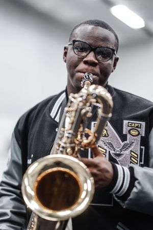 Musician in varsity jacket playing trumpet during performance in indoor setting with overhead lighting.