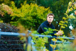 A person sits thoughtfully on a bench surrounded by lush green foliage in a serene garden setting.