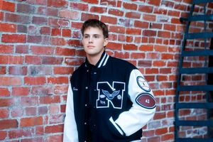 A letterman jacket in black and white with N varsity letter stands against a red brick wall backdrop.