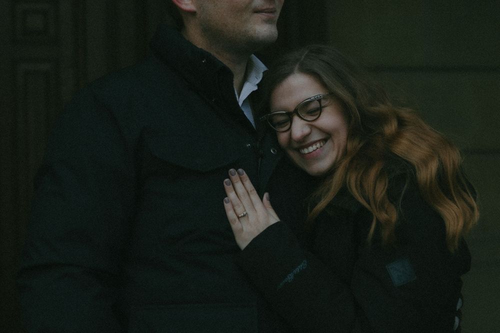 An intimate outdoor portrait shows a couple in dark coats embracing and smiling warmly together.
