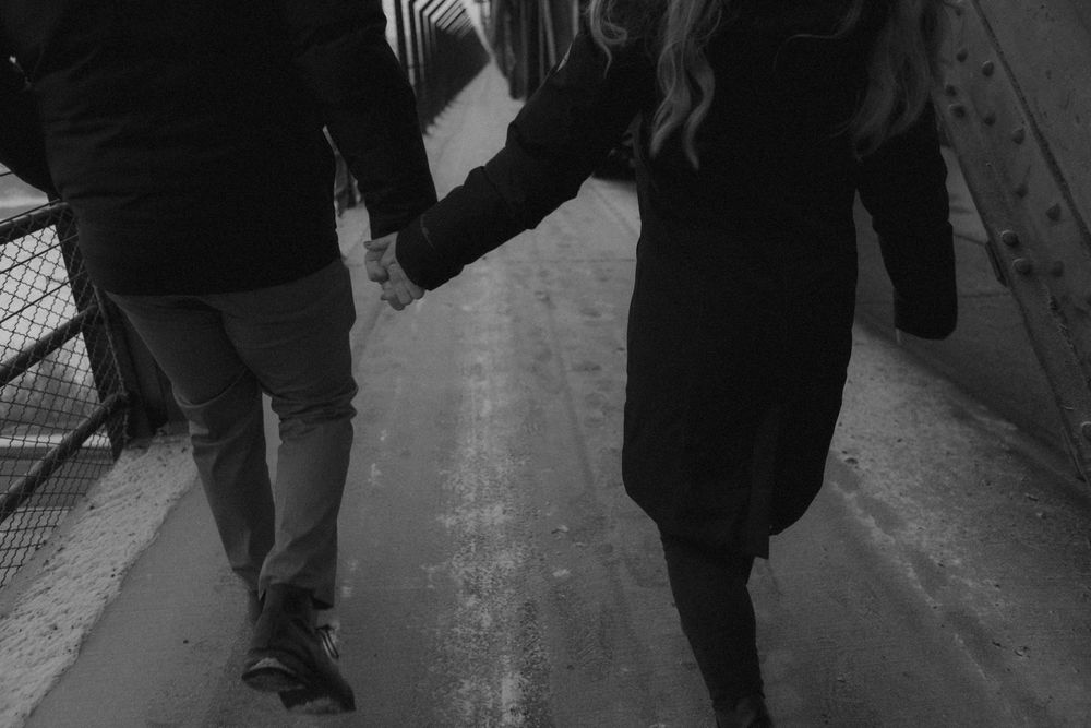 A black and white street photograph shows pedestrians walking in winter coats and boots on a wet sidewalk.