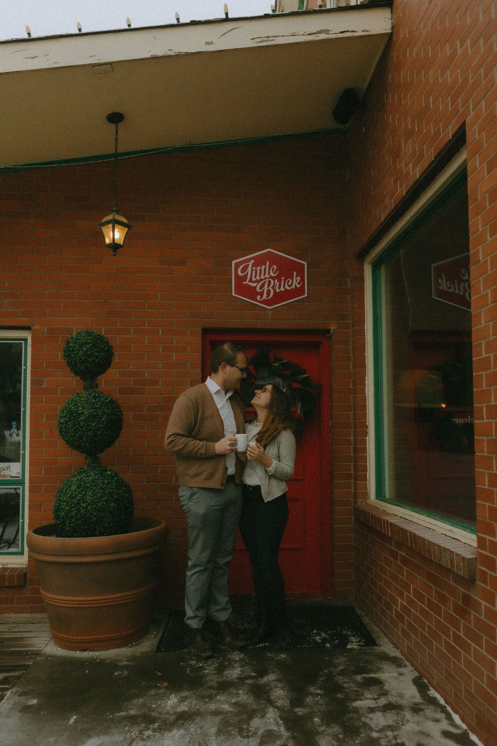 Two people share an intimate moment outside a brick building with a red door and Little Rock sign overhead.