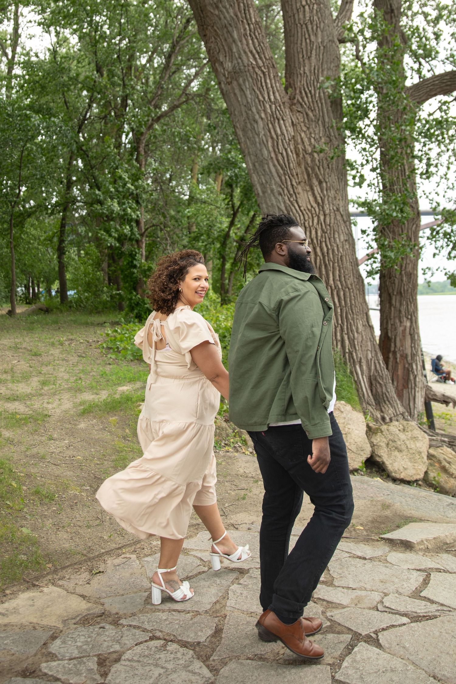 A romantic couple shares tender moments on rocky terrain by the water with trees in the background.