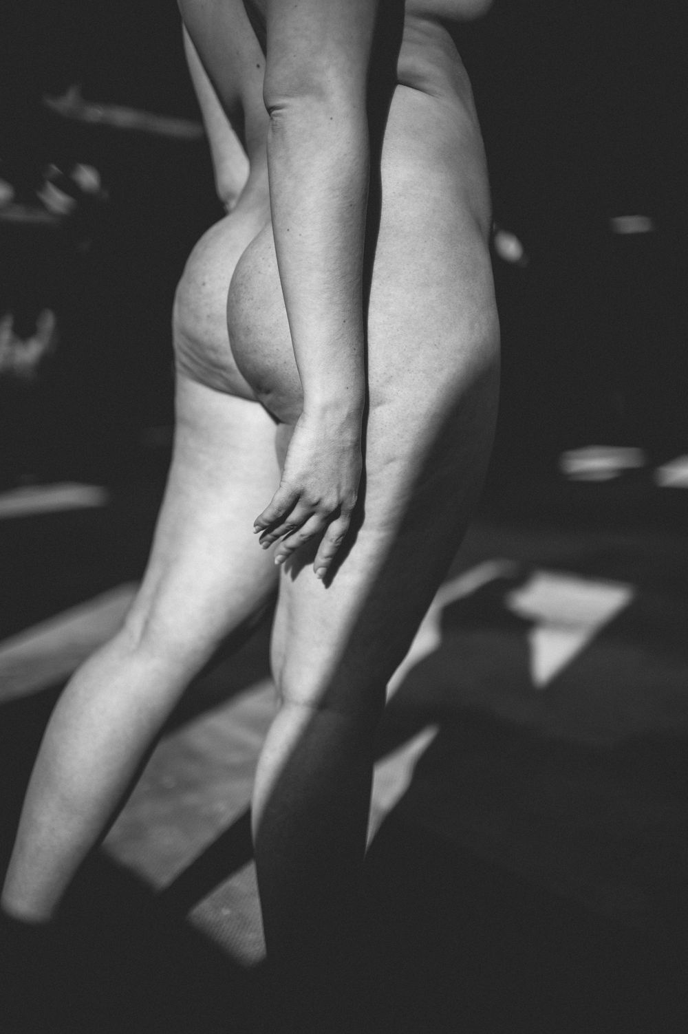 Black and white artistic nude photograph showing a hand touching bare leg with dramatic shadow patterns across the body.