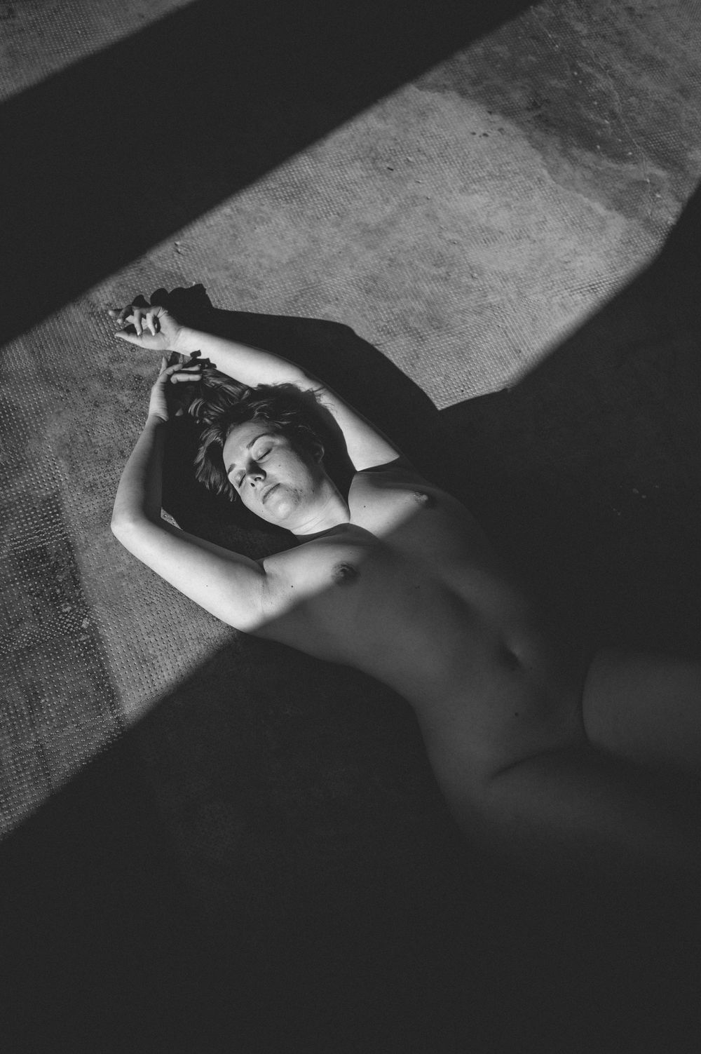 A dramatic black and white photo series captures light and shadow patterns cast across a reclining figure.