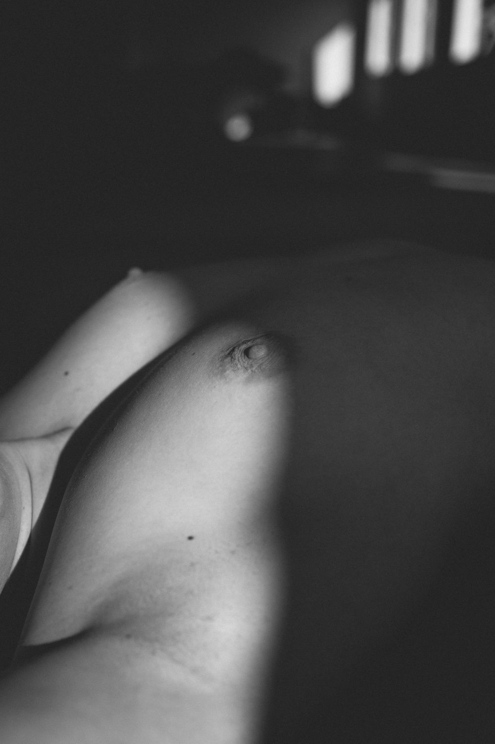 A black and white artistic photograph of bare shoulders with dramatic lighting and shadows creating a sculptural effect.