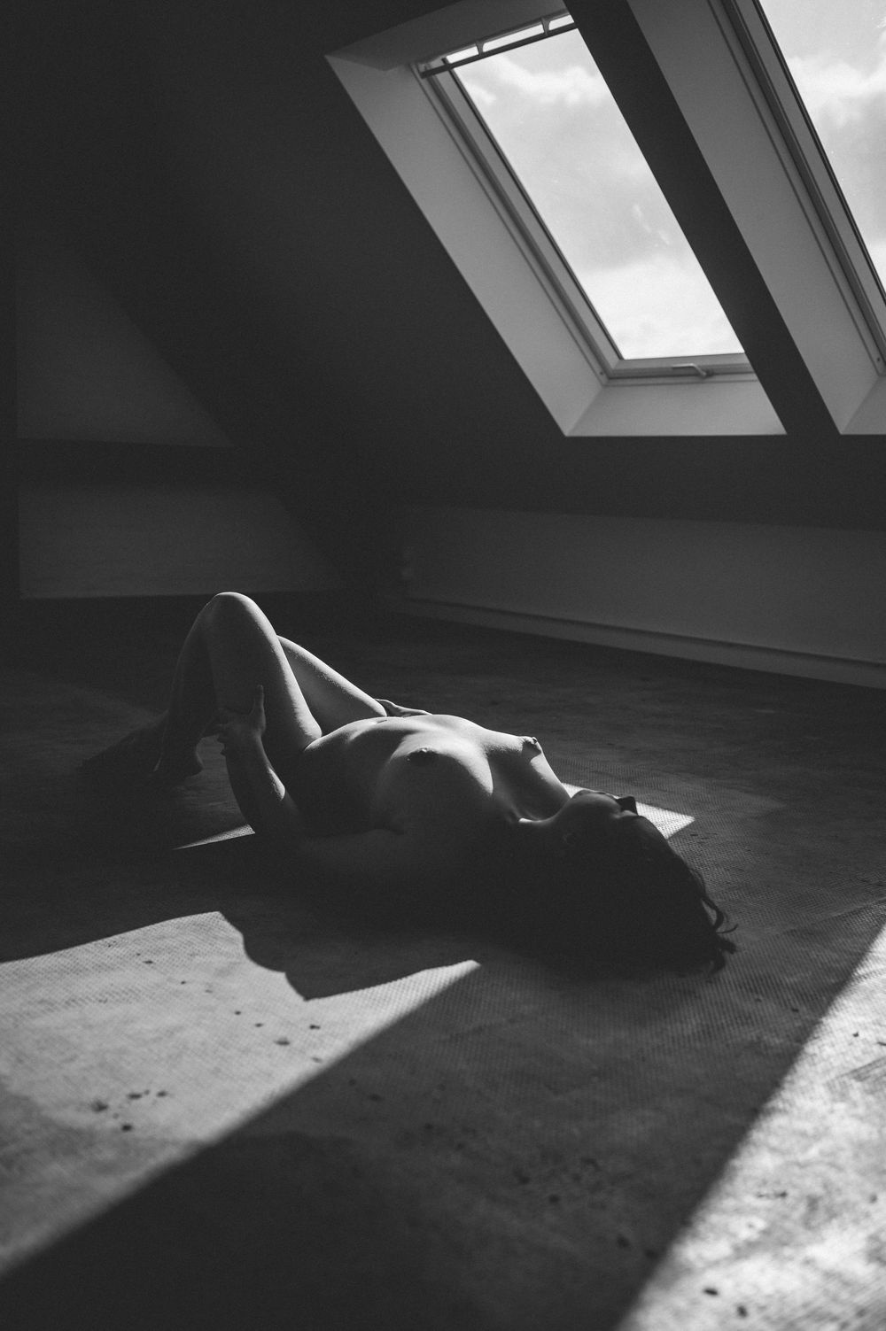 A moody black and white artistic photograph of a silhouette resting in natural light from a skylight window.