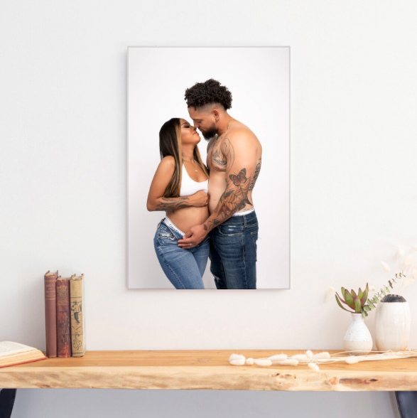 Maternity portrait canvas print displayed on wall above wooden shelf with books and potted plant decoration.