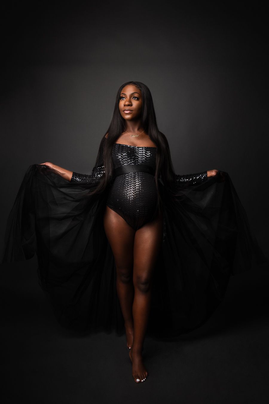 A joyful portrait of someone wearing an elegant royal blue pleated halter dress against a dark brown background.