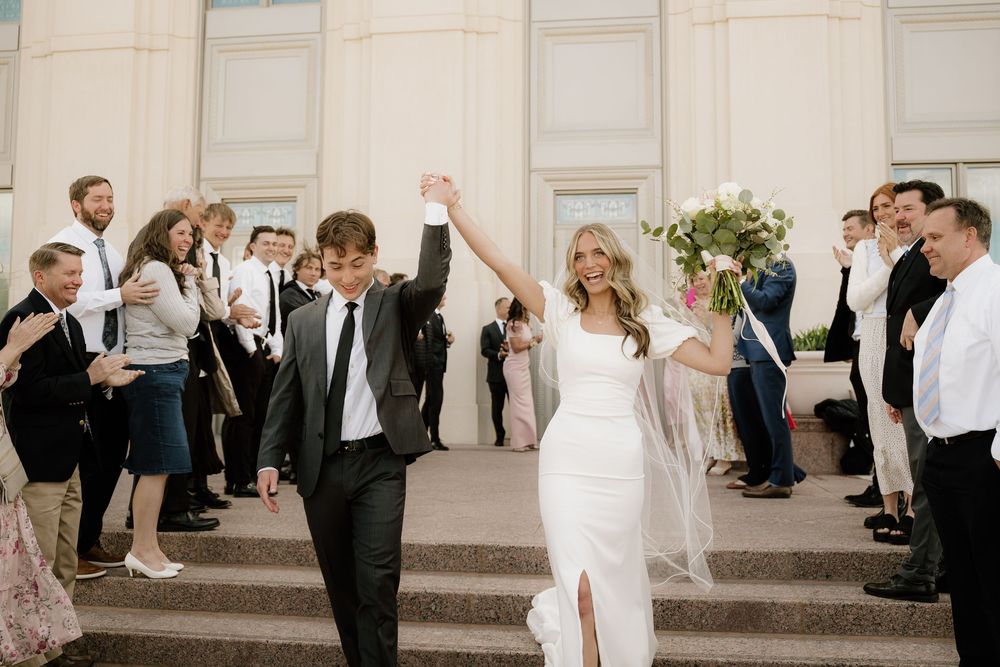 Newlyweds exit through a crowd of cheering guests on stone steps.