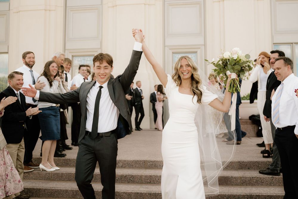 Newlyweds exit their ceremony with raised arms while guests form a pathway outside church.